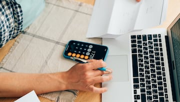 Unrecognizable person counting expenses on calculator in mobile phone app, checking her energy bills at home. Budget management, price increases, inflation, rise in price of products and utilities. View from above, managing home finances using smart phone
