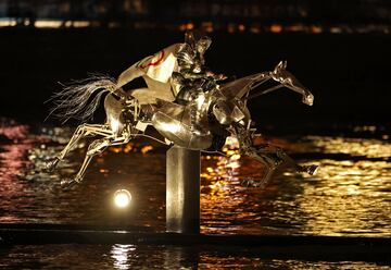 Una jinete cabalga a lomos de iun caballo metálico con una capa  con los aros olímpicos al caer la noche el río Sena.