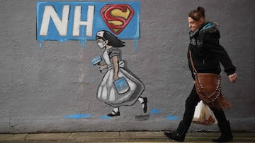 A pedestrian walks past graffiti depicting the badge of the fictional super heros Superman and Superwoman, and Britain&#039;s National Health Service (NHS) logo above street art of a nurse, on a wall in Pontefract, northern England on April 3, 2020, as li