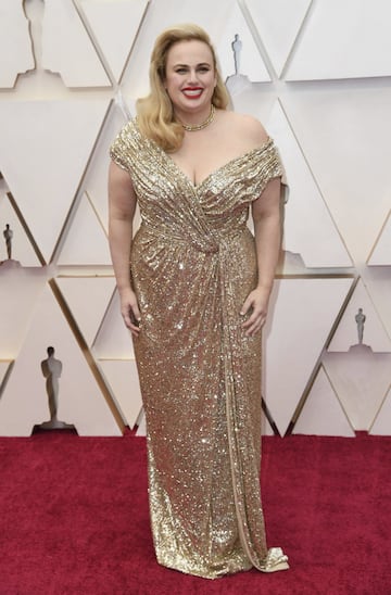 La actriz Rebel Wilson con un diseño de Jason Wu. Es nuestra curvy favorita. Va perfecta. Con el pelo recogido hacia un lado. El vestido es de lentejuelas dorado, lleva un collar de oro y los zapatos también son dorados. 
