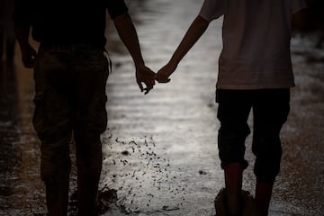 Una pareja de voluntarios camina de la mano por una calle embarrada en una zona inundada en Masanasa, Valencia.