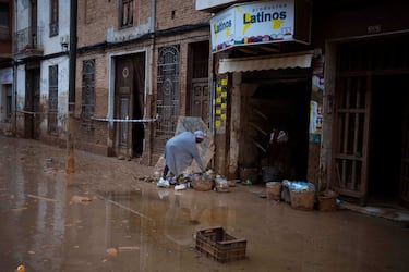 Una mujer recoge alimentos de una canasta colocada afuera de una tienda de comestibles en una calle afectada por las inundaciones en Masanasa, Valencia.