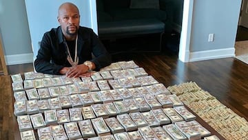 El exboxeador estadounidense Floyd Mayweather sentado en una mesa llena de fajos de billetes.