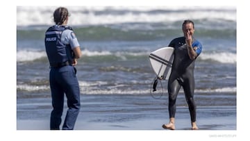 Un surfista hace una peineta a un fot&oacute;grafo que le saca una foto por saltarse la cuarentena por coronavirus en una playa de West Auckland, Nueva Zelanda. 