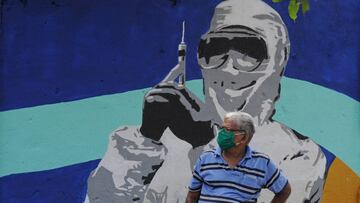 Un hombre con mascarilla ante un mural de un trabajador m&eacute;dico en Bombay