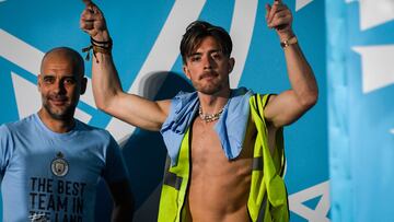 Manchester City's English midfielder Jack Grealish (R) celebrates next to Manchester City's Spanish manager Pep Guardiola (L) on stage following an open-top bus victory parade for their European Cup, FA Cup and Premier League victories, in Manchester, northern England on June 12, 2023. Manchester City tasted Champions League glory at last on Saturday as a second-half Rodri strike gave the favourites a 1-0 victory over Inter Milan in a tense final, allowing Pep Guardiola's side to complete a remarkable treble. Having already claimed a fifth Premier League title in six seasons, and added the FA Cup, City are the first English club to win such a treble since Manchester United in 1999. (Photo by Oli SCARFF / AFP)