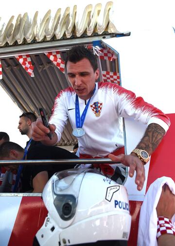 Forward of the Croatian national football team Mario Mandzukic gives an autograph on a local police helmet at the Zagreb International Airport from their open-roof coach during a welcome ceremony on July 16, 2018 in Zagreb.  / AFP PHOTO / ATTILA KISBENEDE