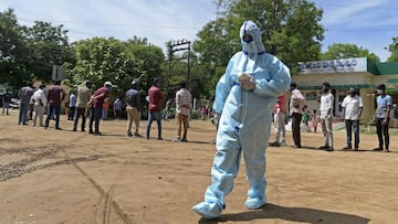 A health worker wearing Personal Protective Equipment (PPE) gear walks past the residents standing in queue to register their names at a free testing centre for the COVID-19 coronavirus, at Medchalx96Malkajgiri district on the outskirts of Hyderabad July 