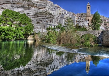 Las casas blancas de Alcalá del Júcar han sido construidas como si se deslizaran por la ladera de una de las hoces del propio río, que avanza irrefrenable por debajo del puente romano que se aprecia en la fotografía. Un castillo, la iglesia de San Andrés o diversas cuevas son algunos de los lugares que no puedes dejar de visitar.