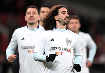 En el calentamiento, los jugadores saltan al campo luciendo una camiseta solidaria con el mensaje 'Jugamos por vosotros' en la parte frontal. Debajo del mensaje aparecen las banderas de las dos comunidades afectadas, la Valenciana y la de Castilla-La Mancha. En la parte de atrás figuran los nombres de los municipios afectados. En la imagen, Marc Cucurella y Mikel Oyarzabal.