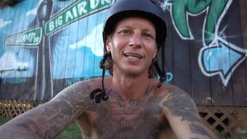 El rider de BMX Ryan Guettler sin camiseta, mirando a cámara y con el casco puesto frente a un muro de madera.