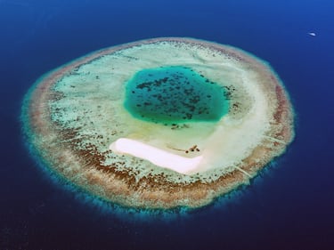 Vista aérea de un pequeño atolón con una hermosa playa de arena en la zona del Atolón Ari Sur. Desde arriba, el atolón parece el iris de un ojo. Atolón Ari Sur, República de Maldivas.
