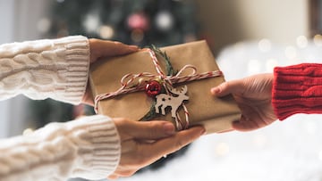 Woman in sweater giving a wrapped Christmas gift box to child. Glowing snow bokeh, fir tree. Winter holidays. NAVIDAD REGALOS REGALO