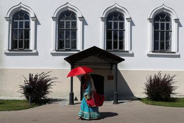 Una mujer vestida con un traje tradicional se protege del sol con un paraguas mientras camina por el Kremlin de Kazan.