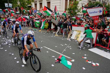Ciclistas del equipo Israel Premier Tech pasan delante de aficionados con banderas palestinas.