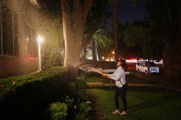 Una mujer riega el rea frente a su casa mientras un incendio forestal arde en el vecindario de Pacific Palisades.