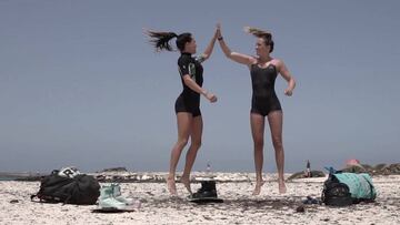 Las kitesurfistas Rita Arnaus y Julia Castro, con neopreno corto, saltando y chocando la mano en una playa de Fuerteventura (Islas Canarias) este mes de julio del 2020.