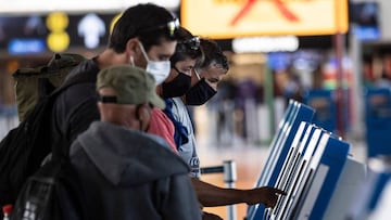 Passengers wear face masks while printing their boarding pass at Santiago International Airport, in Santiago, on April 20, 2020 during the new coronavirus, COVID-19, pandemic. - Latin America&#039;s biggest airline, the Brazilian-Chilean group LATAM, announced last Friday that the 95% reduction of its passenger operations announced in April will be extended until May due to the coronavirus crisis, which will cause a deeper impact than expected. (Photo by MARTIN BERNETTI / AFP)