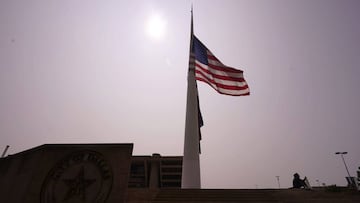 Kyle A.B., right, holds a protest sign under a hazy sky as flags fly at half staff in front of Dallas City Hall in memory of Supreme Court Justice Ruth Bader Ginsburg, Saturday, Sept. 19, 2020, in Dallas. (AP Photo/LM Otero)