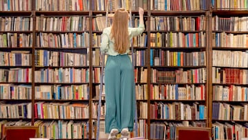 Una mujer busca un libro subida en la escalera de madera de la biblioteca en Sant Cugat, Espa?a.