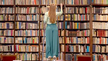 Una mujer busca un libro subida en la escalera de madera de la biblioteca en Sant Cugat, España.