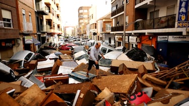 Un hombre intenta avanzar sobre una calle llena de vehículos amontonados  en el área de Sedaví en Valencia, España.