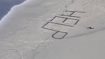 Un surfista tumbado e inconsciente al lado de la palabra HELP escrita en la arena de una playa de Auckland (Nueva Zelanda) en febrero del 2021.