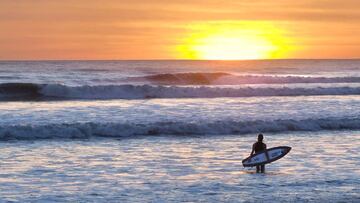 El surfista vasco Kepa Acero frente a una ola y la puesta de sol, con su tabla de surf y su neopreno, dispuesto a surfear.