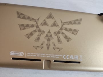 El emblema de la Familia Real de Hyrule viste la parte posterior de la consola. Un símbolo que todo fan de la franquicia conoce a la perfección, surgido a partir de la Diosa Hylia, de ahí la forma de ave (pelícaro).