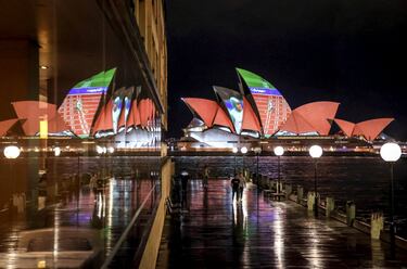 Unas personas observan la fachada de la Ópera de Sídney, que aparece iluminada de noche con una proyección de la exatleta olímpica Cathy Freeman. El motivo no es otro que la celebración del vigésimo aniversario de la medalla de oro de la exdeportista australiana en la prueba de 400m lisos en los Juegos Olímpicos de Sídney 2020. 