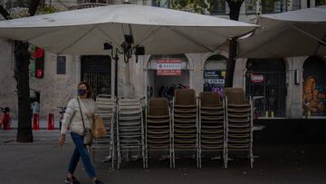 Una mujer pasa junto a la terraza recogida de un bar cerrado durante el cuarto día de la entrada en vigor de las nuevas restricciones en Cataluña, en Barcelona, Cataluña (España) a 20 de octubre de 2020. El pasado viernes 16 de octubre entraron en vigor las nuevas restricciones decretadas por la Generalitat por el coronavirus. Entre ellas, se paraliza la actividad durante dos semanas en bares restaurantes, se suspende la actividad deportiva no profesional dos semanas, se cierran las áreas de juego infantil a las 20.00h, se suspende la apertura al público de juegos, casinos y bingos, se reduce el 50% del aforo en zonas comunes de hoteles y también en cines y restaurantes, y se reduce al 30% el aforo en comercios superiores a 400 metros cuadrados y centros comerciales.
20 OCTUBRE 2020 CORONAVIRUS;COVID-19;PANDEMIA;ECONOMÍA;CRISIS
David Zorrakino / Europa Press
20/10/2020