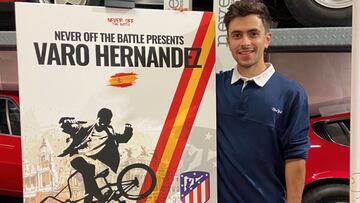 El rider de BMX Flatland Varo Hernández posa junto a un cartel con su nombre y su silueta, el escudo de Madrid y la bandera de España en un garaje con varios coches Ferrari rojos al fondo.