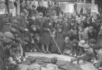 1936, los niños de la escuela Wood Lane escuhan atentamente a la maestra mientras les explica en qué consiste la regata sobre una maqueta en el suelo.