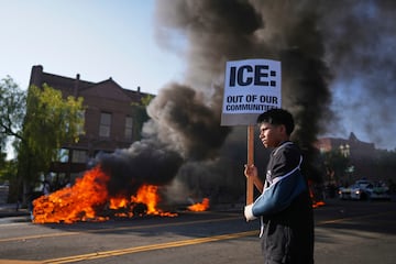 Un manifestante sostiene un cartel mientras un taxi se incendia cerca del centro de detención metropolitano del centro de Los Ángeles.