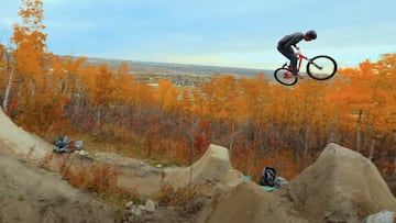Rider de MTB saltando en unos saltos de tierra en Substrata, Canadá, con los árboles de colores otoñales