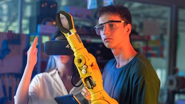 Teens doing experiments in robotics in a laboratory. Boy in protective glasses looking at a robot controlled by a girl hand. Red and blue illumination