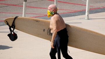 Un surfista deja la playa con un pa&ntilde;uelo tap&aacute;ndole la cara a modo de mascarilla durante la pandemia de coronavirus que afecta a pa&iacute;ses como Espa&ntilde;a o Estados Unidos. En la playa de Encinitas, California, en abril del 2020. 