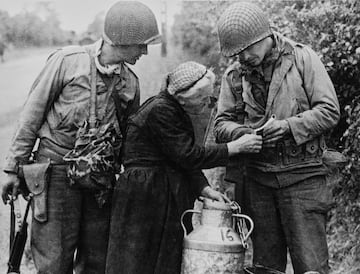 El soldado Carl Rendleman, Primer Ejército de los Estados Unidos, utiliza un libro de frases francés-inglés para explicar a una mujer francesa local que no puede pasar por la carretera N13 Montebourg - Sainte-Mère-Église después de la Operación Overlord.