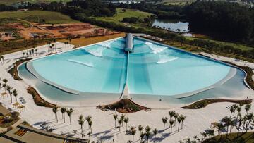 Así la visión frontal del Wavegarden Praia da Grama (Brasil) visto desde el aire. Con olas de la tecnología Cove rompiendo, algunas palmeras y el bosque al fondo.