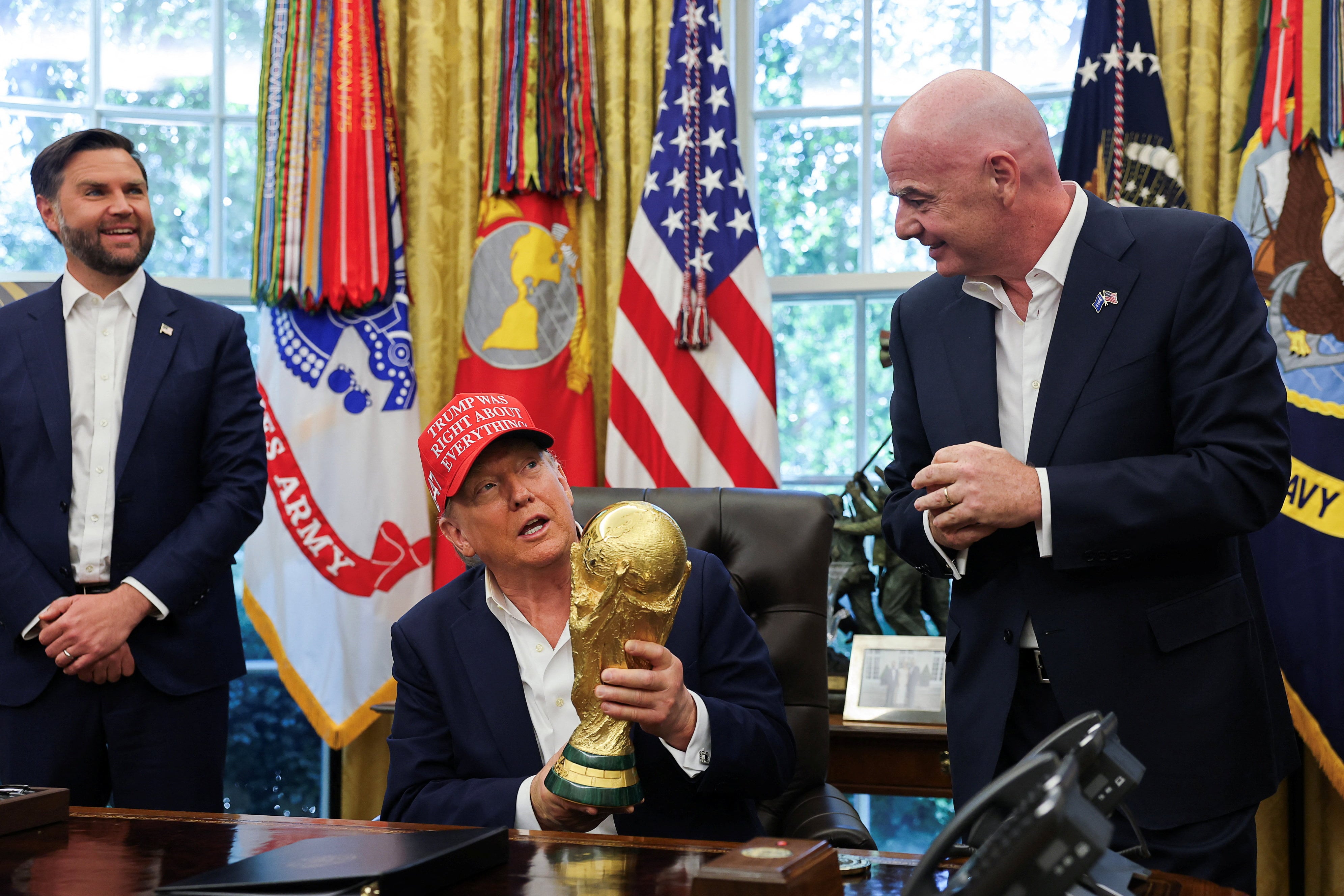 U.S. President Donald Trump holds the FIFA World Cup Trophy, while he makes an announcement on the 2026 FIFA World Cup, as U.S. Vice President JD Vance and FIFA president Gianni Infantino stand, in the Oval Office at the White House in Washington, D.C., U.S., August 22, 2025. REUTERS/Jonathan Ernst