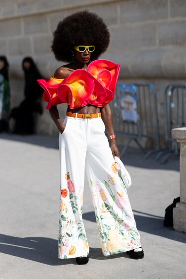 Una invitada luce gafas de sol amarillas, un cinturón de piel naranja de Hermès, un top corto con volantes rosa y amarillo, un bolso de piel blanco, calcetines blancos, sandalias negras de plataforma y pantalones blancos de cintura alta con estampado floral en el exterior del desfile de Dior durante la Semana de la Moda de París Primavera/Verano 2026, el 1 de octubre de 2025.