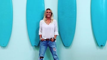 Lisa Andersen, con las manos en los bolsillos, frente a una pared con tablas de surf azules. 