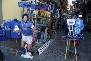 En Nápoles se respira fútbol con motivo del encuentro entre el conjunto italiano y el Barça. Y como no podía ser de otra manera, la figura de Maradona, quien vistió las camisetas de ambos clubes, sigue muy presente en las calles de la ciudad. Bufandas conmemorativas del partido, elásticas del ‘10’ y hasta una foto a tamaño natural del crack argentino.