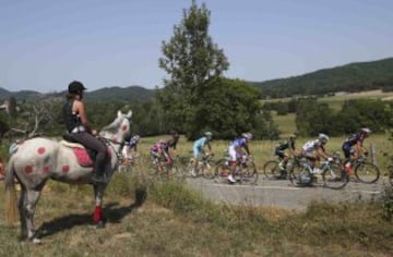 Una mujer montada a caballo pintado con lunares rojos observa la etapa de hoy.