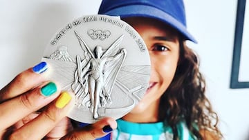 La skater brasile&ntilde;a Rayssa Leal ense&ntilde;a su medalla de plata de los Juegos Ol&iacute;mpicos de Tokio 2020 (Skate Street Women) a c&aacute;mara, sujetada con una mano con las u&ntilde;as pintadas de los colores de Brasil y con media cara suya saliendo por detr&aacute;s, sonriendo, con una gorra tambi&eacute;n de Brasil. 