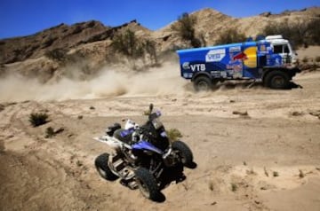 Airat Mardeev y los copilotos Aydar Belyaev y Dimitry Svistunov del equipo KAMAZ pasan junto al vehículo abandonado del argentino Pablo Coperri.