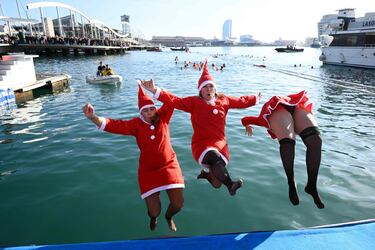 Participantes vestidos con trajes de Santa Claus saltan al agua en el puerto de Barcelona.