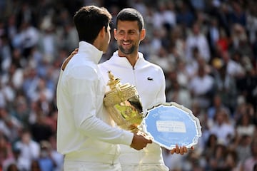 Carlos Alcaraz y Novak Djokovic charlan amistosamente con sus respectivos trofeos de Wimbledon.