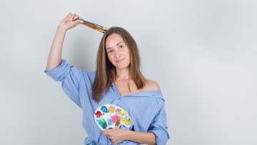 Young woman holding painting tools in blue shirt, shorts and looking hopeful. front view.
