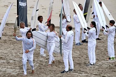El surfista francés Edouard Delpero (izquierda) sostiene la llama olímpica, flanqueado por la surfista Zoe Grospiron (centro) durante el relevo de la antorcha en la playa entre Biarritz y Anglet.